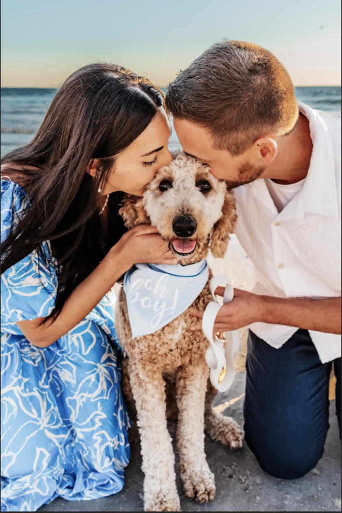 a couple kisses their poodle on the head during their beach engagement session